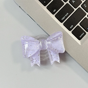 Macro shot of glittery purple bow phone grip on a silver metallic laptop surface