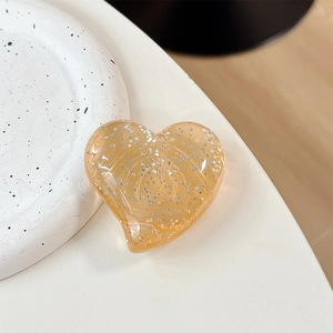Macro detail of amber heart phone grip with sparkling silver glitter on white surface