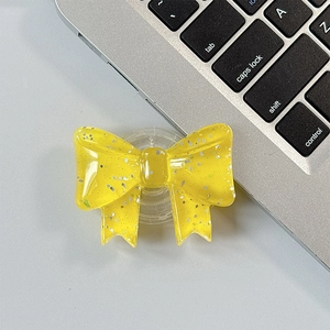 Close-up of a glittery yellow bow-shaped collapsible phone grip on a grey desk