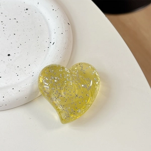Detailed view of yellow transparent glitter heart phone stand on a white ceramic tray