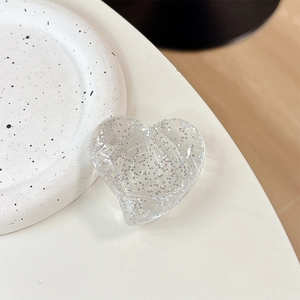 Macro detail of transparent heart phone grip with sparkling silver glitter on white desk