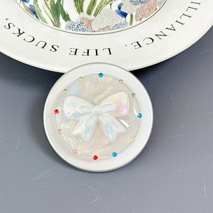 Close-up of shell-textured bowknot phone grip with colorful rhinestones on a white plate