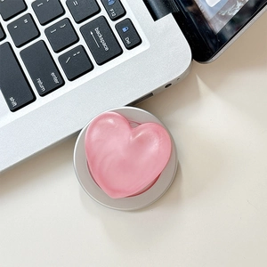 Pink heart-shaped phone grip with pearl finish and silver base on laptop keyboard
