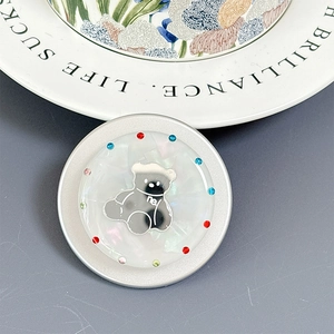 Detail of shell texture phone grip with rhinestones and cartoon bear on ceramic plate
