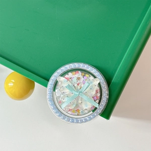 Detail of a round phone grip featuring a blue ribbon bow and colorful heart sequins