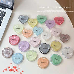Magnetic heart-shaped phone grip stand in various pearl colors on a white desk