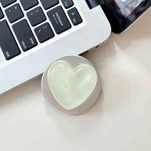 Close-up of light green heart-shaped phone grip with matte finish on a white desk