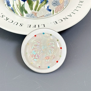 Close-up of a circular MagSafe phone grip with shell texture and rhinestone bow detail