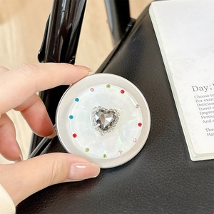 Detail of magnetic phone socket with heart gem and colorful rhinestones on shell texture