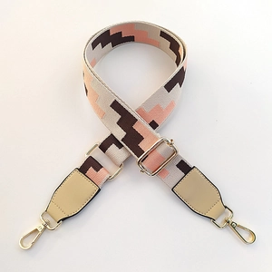 Close-up of beige and pink geometric woven bag strap with golden metal hooks