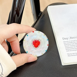 Macro view of a round marble phone grip featuring a red heart rhinestone and colorful crystals