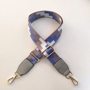 Detail of adjustable woven bag strap with geometric patterns and gold metal lobster clasps