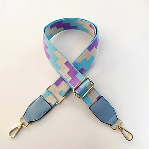 Detail of colorful geometric woven bag strap with blue leather ends and gold lobster clips