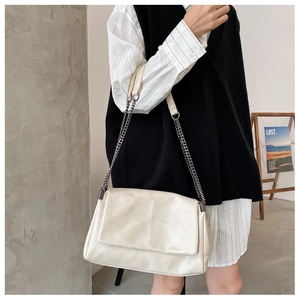 Close-up of quilted cream faux leather messenger bag with silver chain strap and flap