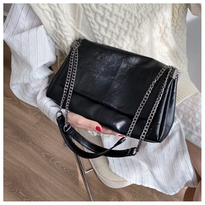 Detail of black vintage messenger bag with glossy cracked leather and silver chain strap