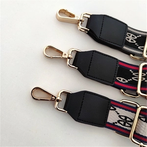 Detail of adjustable bag strap with green and red stripes and gold metal buckles