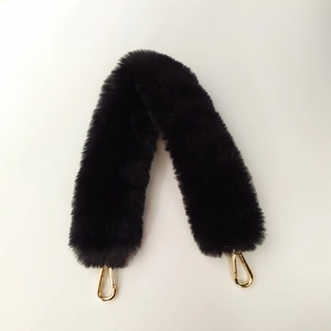 Détail d'une bandoulière en fausse fourrure noire duveteuse avec mousquetons en métal doré