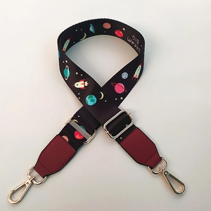 Detail of space-themed bag strap featuring rockets and planets with gold metal buckles