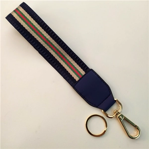 Detail of red and green striped fabric strap with blue faux leather and gold metal clip