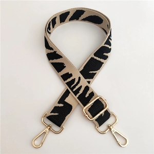 Close-up of adjustable beige canvas strap with black patterns and gold metal swivel hooks