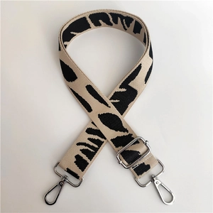 Close-up of adjustable woven canvas strap with beige jacquard pattern and silver hooks