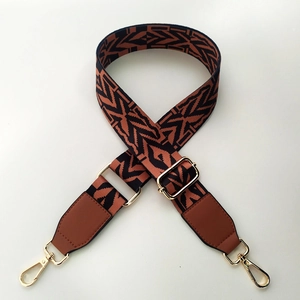 Detail of adjustable wide canvas strap with orange and black geometric weaving and gold clasp