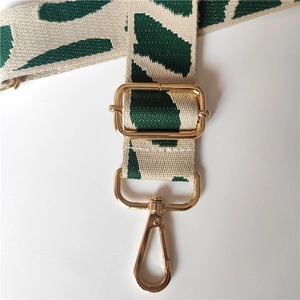 Detail of adjustable green and beige woven bag strap with golden metal lobster clasps