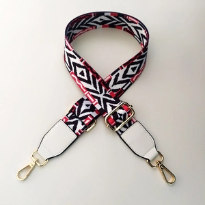 Detail of adjustable wide bag strap with red and black geometric pattern and gold hardware