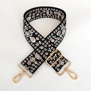 Close-up of wide embroidered bag strap with floral patterns and gold metal hardware