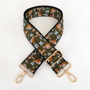 Close-up of floral embroidery on wide adjustable bag strap with gold metal hooks