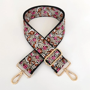 Macro detail of wide embroidered floral bag strap with gold lobster claw metal clasps