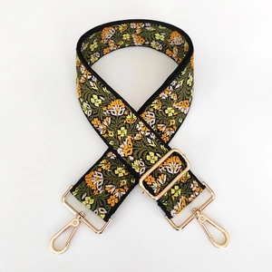 Close-up of yellow floral embroidery on wide black bag strap with gold metal buckles