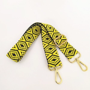 Detail of adjustable woven purse strap with yellow and black geometric patterns and gold clips
