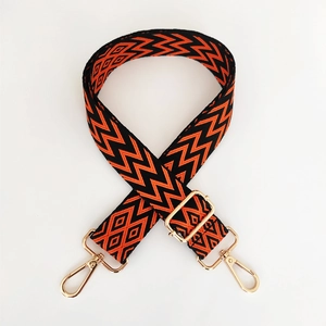 Detail of adjustable woven bag strap in orange and black with gold metal hooks