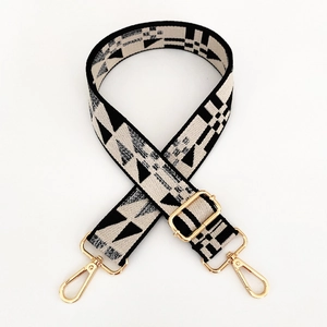 Detail of adjustable geometric patterned woven bag strap with golden metal clasps