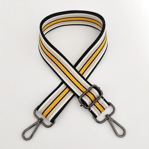Detail of adjustable canvas bag strap with yellow, black, and white stripes and metal hardware