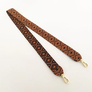 Close-up of wide ethnic woven bag strap with brown geometric patterns and gold clasps