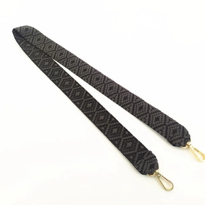 Close-up of black and grey geometric patterned jacquard bag strap with gold metal buckles