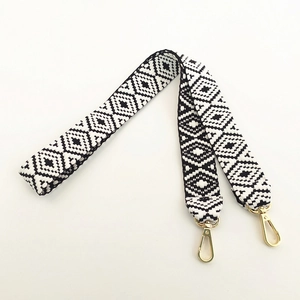 Detail of wide black and white geometric diamond woven shoulder strap with gold hooks