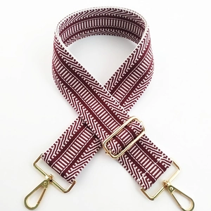 Detail of burgundy embroidered wide bag strap with golden rotating metal hooks