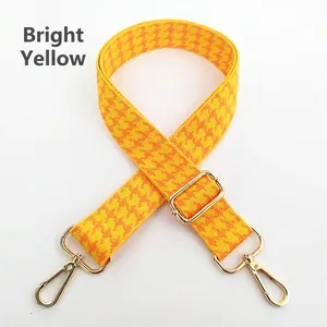 Close-up of bright yellow houndstooth bag strap with adjustable gold buckle and metal swivel hooks