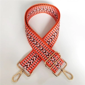 Detail of vibrant orange embroidered bag strap with geometric V-patterns and gold metal clasps
