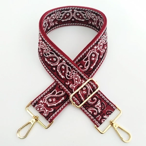 Close-up of red paisley embroidered wide bag strap with polished gold metal lobster clasps