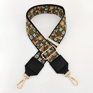 Close-up of olive green floral embroidery strap with gold buckles and black leather ends
