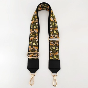 Close-up of floral embroidery on wide adjustable canvas bag strap with gold metal hooks