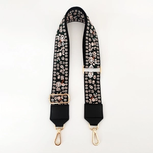 Close-up of floral embroidery on wide fabric bag strap with golden metal hardware