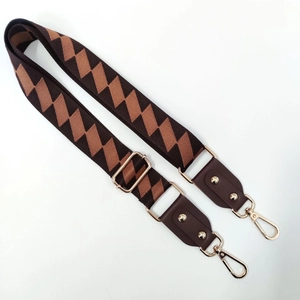 Detail of adjustable wide shoulder strap with brown geometric patterns and gold clips