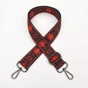Detail of embroidered adjustable bag strap with red floral pattern and metal hooks
