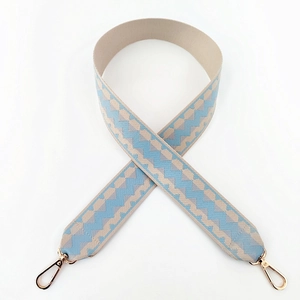 Detail of wide woven strap with blue and beige geometric pattern and gold swivel hooks