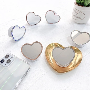 Close-up of heart-shaped mirror phone grips with colorful rhinestones on a white surface